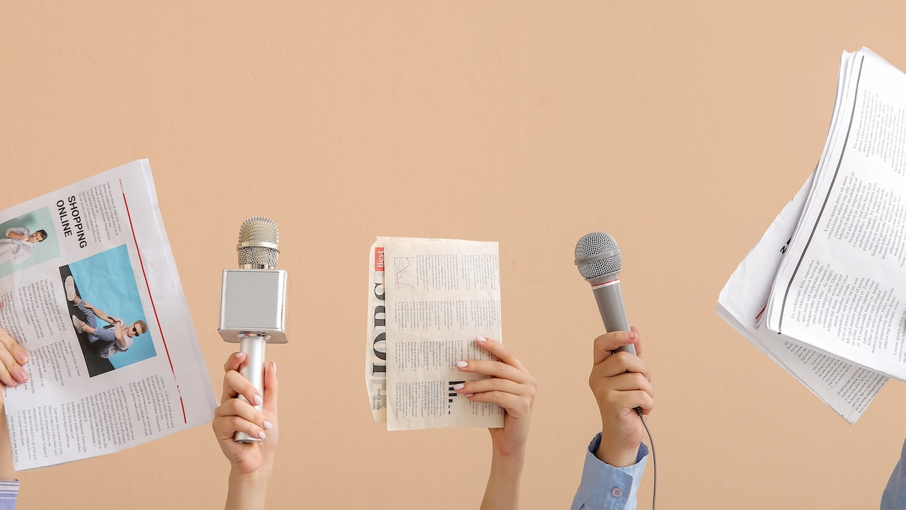 Hände mit Mikrofonen und Zeitungen auf beigem Hintergrund