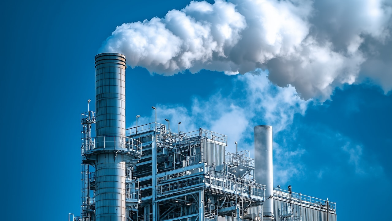 Industrieanlage mit Rauchschwaden aus dem Schornstein vor blauem Himmel