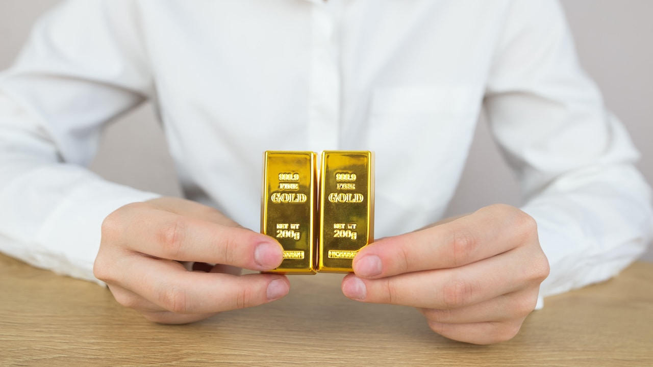 Eine Frau in weißer Hemdbluse hält zwei Goldbarren vor sich