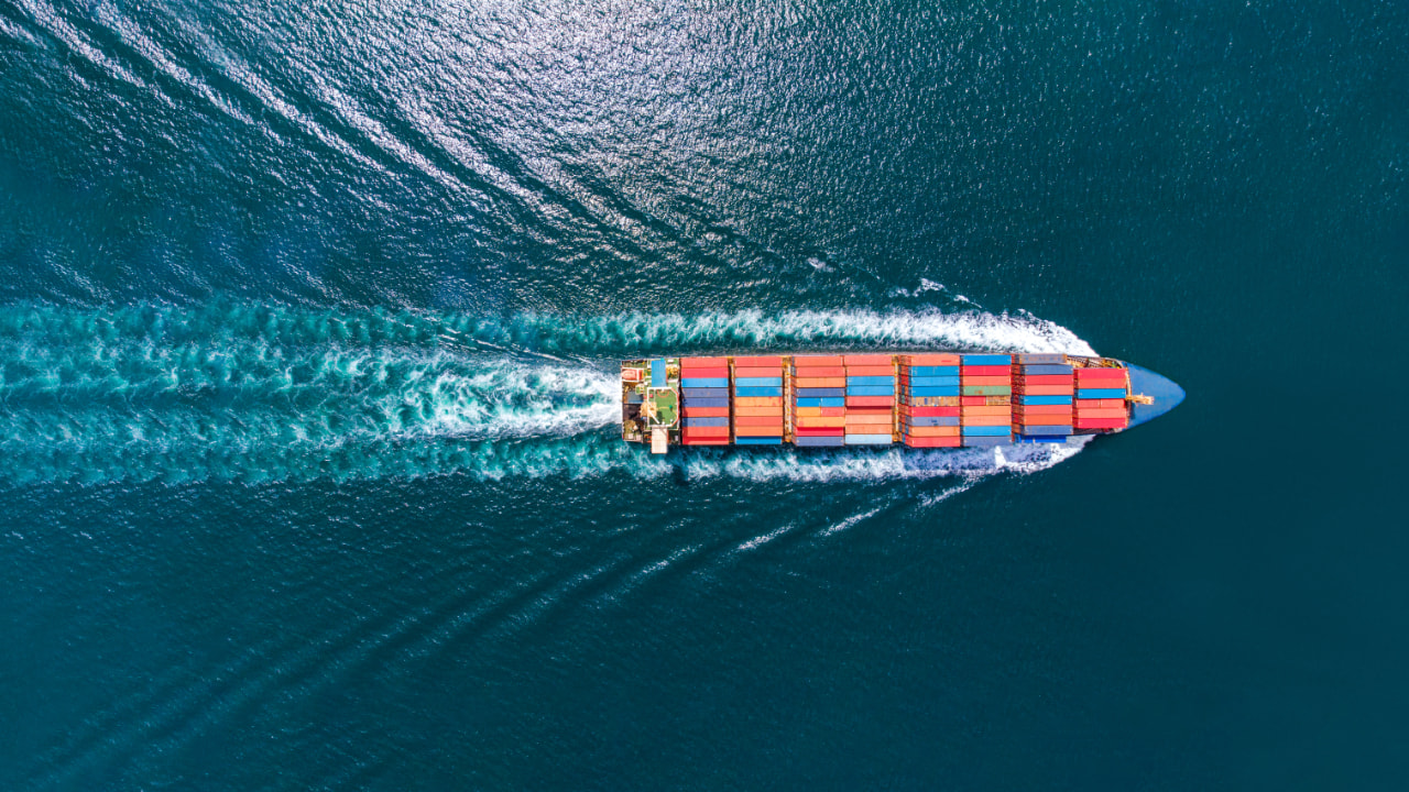 Luftaufnahme eines Frachtschiffs im Ozean, das vielen Containern transportiert, senkrecht von oben fotografiert