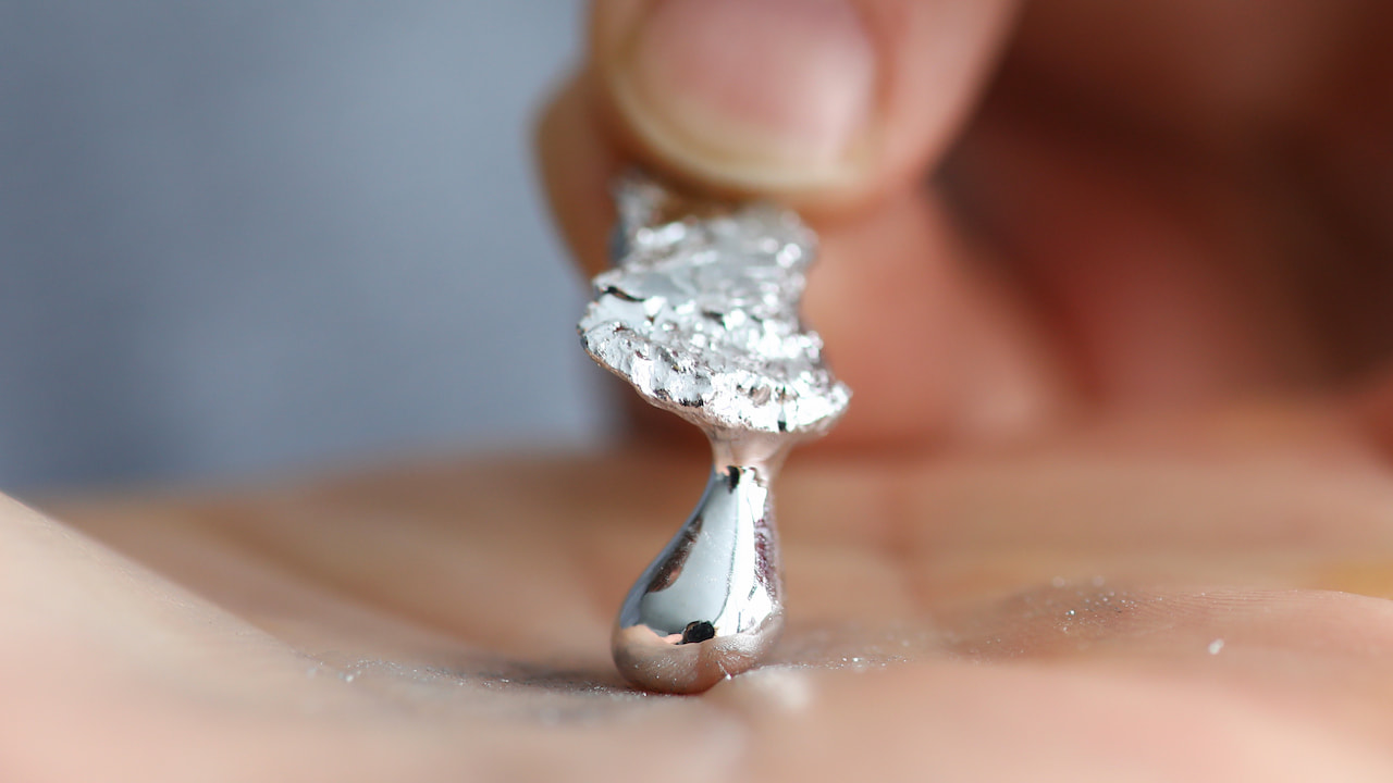 Nahaufnahme des Technologiemetalls Galliums in flüssigem Aggregatzustand mit einer männlichen Hand