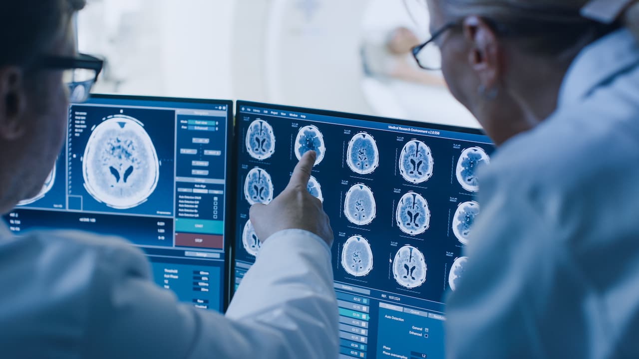In der Kontrollkammer diskutieren Arzt und Radiologe Diagnostik während des Analyseverfahrens und Monitore, die Ergebnisse von Gehirnscans zeigen, im Hintergrund durchläuft der Patient MRI- oder CT-Scan-Verfahren.